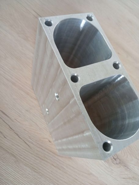 Bloc en métal avec deux cavités, surface polie et plusieurs vis sur les côtés.